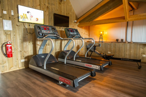 Moderne fitnessruimte in een glamping vakantiepark met twee loopbanden, een roeimachine en houten interieur.