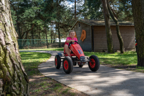 Kind rijdt op een rode trapauto op een pad in het bos bij Recreatiepark Keiheuvel in Antwerpen, België.