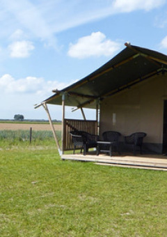Tienda safari con porche y sillas en Minicamping de Vrolijke Flierefluiter en Países Bajos, vista al campo.