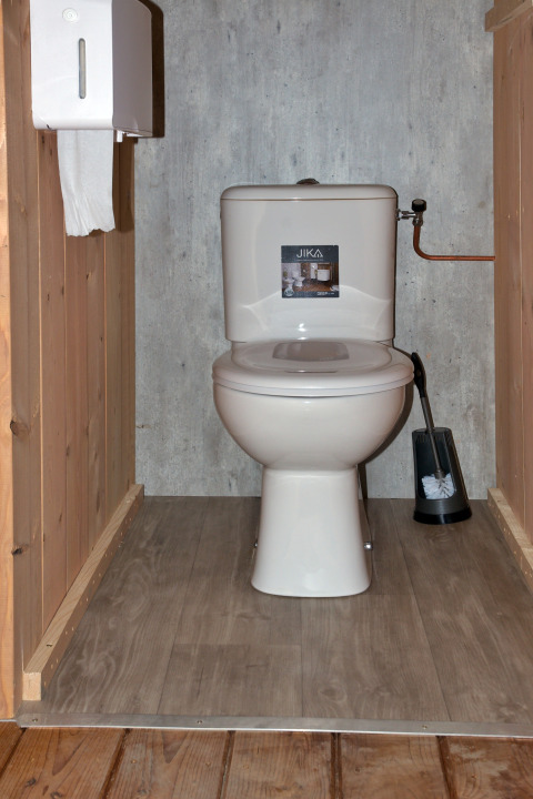Photo d’une toilette dans une tente safari, avec sol en bois, porte-papier mural et brosse WC.