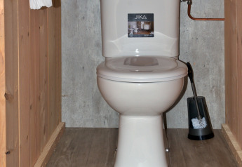 Foto van een toilet in een safaritent met houten vloer, wandtoiletrolhouder en wc-borstel.