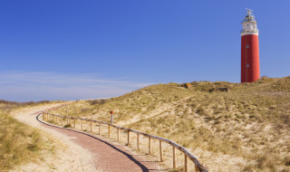 Faro rojo junto a un sendero sinuoso entre dunas, ideal para glamping en un parque vacacional tranquilo.