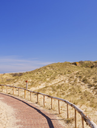 Faro rojo junto a un sendero sinuoso entre dunas, ideal para glamping en un parque vacacional tranquilo.