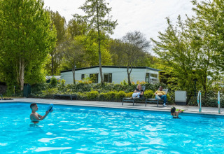 Kinderen spelen in een buitenzwembad terwijl volwassenen ontspannen op ligstoelen bij een glamping vakantiepark.