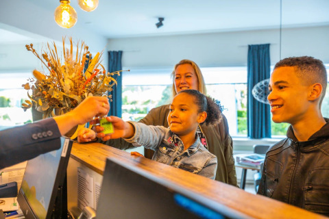 Gezin ontvangt sleutels bij receptie van vakantiepark met glamping, glimlachend, klaar voor hun verblijf.