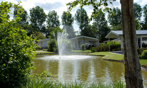 Een rustige vijver met fontein in een vakantiepark, omringd door groene bomen en glamping accommodaties.