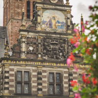 Edificio histórico con fachada ornamentada y flores en primer plano, fotografiado en un día nublado en los Países Bajos.