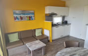 Moderne stue og køkken i Comfort Lodge på Kompas Camping Nieuwpoort, Belgien, med gule vægge og sofa.