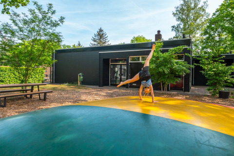 Kind maakt een radslag op een kleurrijk springkussen bij een glampingaccommodatie in een vakantiepark.