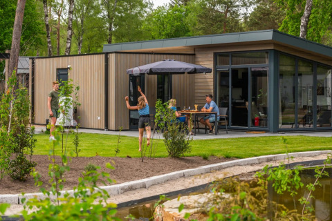 Gezin geniet van glamping op een vakantiepark met moderne lodges, tuin en terras aan een vijvertje.