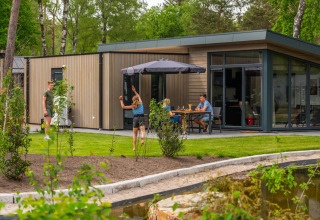 Gezin geniet van glamping op een vakantiepark met moderne lodges, tuin en terras aan een vijvertje.