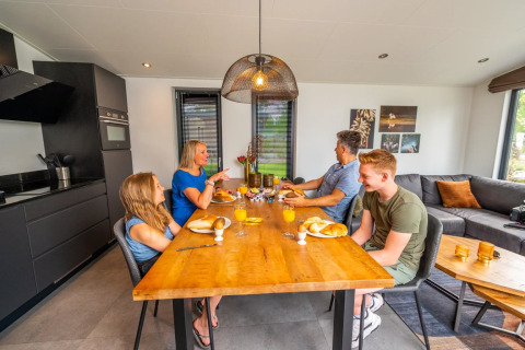 Gezin geniet van ontbijt met verse broodjes en sap aan houten tafel in een luxe glamping accommodatie.
