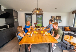 Gezin geniet van ontbijt met verse broodjes en sap aan houten tafel in een luxe glamping accommodatie.