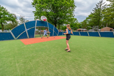 Twee mensen spelen voetbal op een multifunctioneel sportveld in een vakantiepark met glampingaccommodaties.