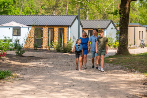 Een gezin wandelt op een zonnige dag door een vakantiepark met moderne glamping accommodaties.