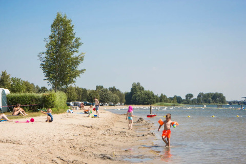 Kinderen spelen op een zandstrand aan het water in een vakantiepark met glampingaccommodaties.