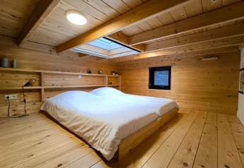 Alloggio glamping moderno con pareti in legno, letto basso, lucernario e arredamento minimalista.