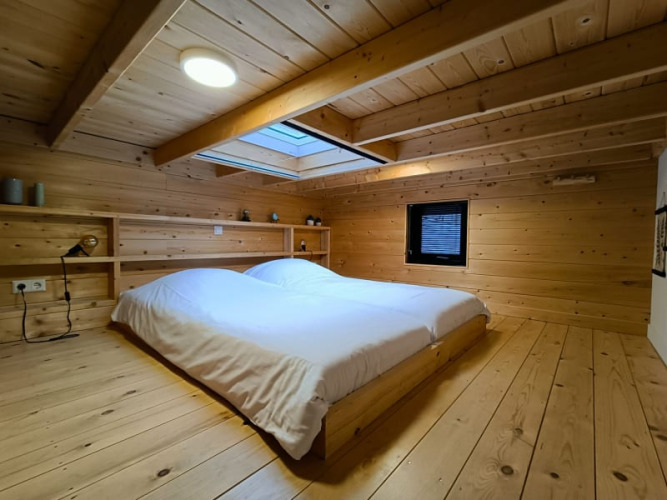 Modernes Glamping-Zimmer mit Holzverkleidung, niedrigem Bett, Dachfenster und minimalistischer Deko.