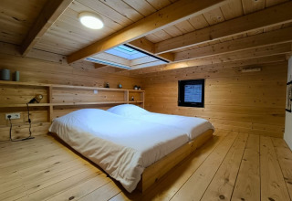 Hébergement glamping moderne avec murs en bois, lit bas, puits de lumière et décoration minimaliste.