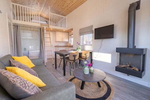 Moderne glampingaccommodatie met zithoek, bank, keuken, eettafel, vide en wandhaard.