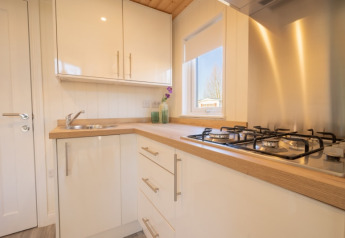 Moderne glampingkeuken met gaskookplaat, gootsteen, lichte kasten en een raam met uitzicht op de natuur.