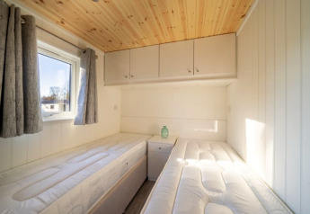 Chambre lumineuse de glamping avec deux lits simples, plafond en bois, fenêtre et placards muraux.