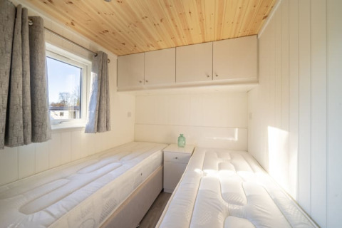Lichte glampingkamer met twee eenpersoonsbedden, houten plafond, raam met gordijnen en bovenkasten.