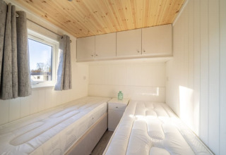 Habitación luminosa de glamping con dos camas individuales, techo de madera y armarios superiores blancos.