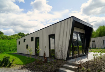 Moderne lodge met schuin dak en grote ramen, omgeven door groen onder een deels bewolkte lucht.