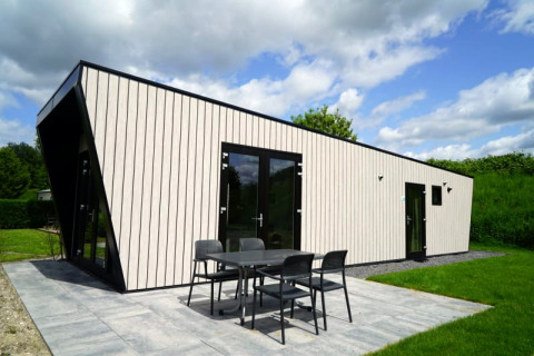 Modernes Lodge mit schwarzen Rahmen, großen Fenstern und Sitzbereich im Garten, umgeben von viel Grün.