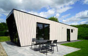 Moderne lodge met verticale gevelbekleding, zwarte accenten en terrasmeubilair in een groene omgeving.