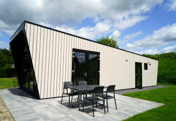 Moderne lodge met lichte gevel, zwarte kozijnen, grote glazen deuren en terras in een groene omgeving.