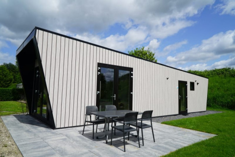 Moderne lodge met lichte gevel, zwarte kozijnen, grote glazen deuren en terras in een groene omgeving.