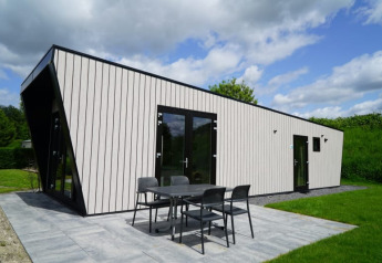 Modernes Lodge mit schwarzen Rahmen, großen Fenstern und Sitzbereich im Garten, umgeben von viel Grün.