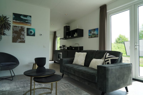 Modernes Lodge-Wohnzimmer mit Sofa, Couchtischen, Wandkunst, Küchenzeile und großen Fenstern.
