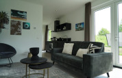 Moderne lodge woonkamer met bank, salontafels, wanddecoratie, kitchenette en grote ramen.