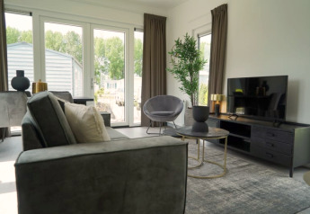 Woonkamer van een lodge met moderne inrichting, grote ramen, flatscreentelevisie en tuinzicht.