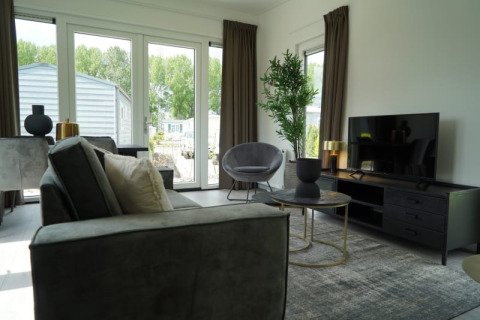 Woonkamer van een lodge met moderne inrichting, grote ramen, flatscreentelevisie en tuinzicht.