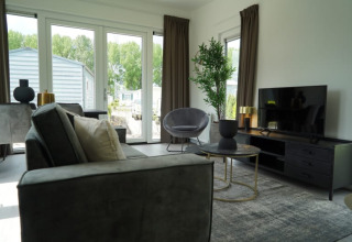 Woonkamer van een lodge met moderne inrichting, grote ramen, flatscreentelevisie en tuinzicht.
