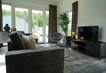 Salon de lodge au décor moderne, grandes fenêtres, mobilier contemporain, télévision et vue sur jardin.