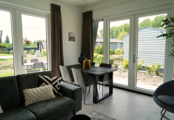 Moderne lodge woonkamer met grote ramen, eettafel, grijze bank en uitzicht op tuin en terras buiten.
