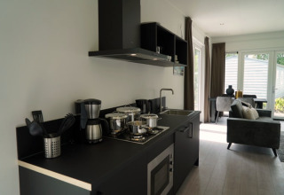 Moderne Küchenzeile in einer Lodge mit Herd, Kaffeemaschine, Topfset und Blick ins Wohnzimmer.