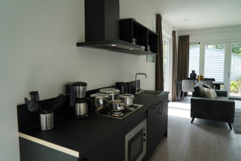 Moderne lodgekeuken met zwart aanrecht, fornuis, koffiezetapparaat en uitzicht op de woonkamer.