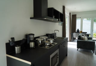 Moderne lodgekeuken met zwart aanrecht, fornuis, koffiezetapparaat en uitzicht op de woonkamer.