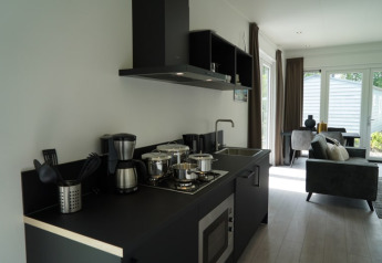 Cuisine moderne de lodge avec mobilier noir, cuisinière, cafetière et vue sur le salon lumineux.