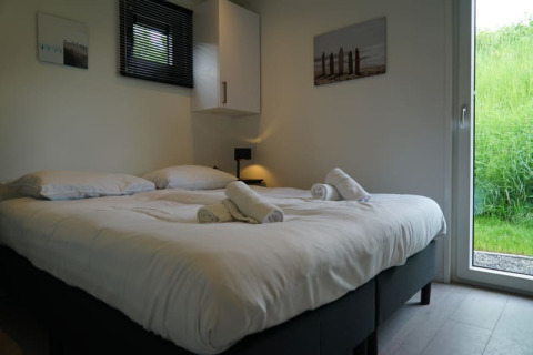 Lichte slaapkamer in een lodge met tweepersoonsbed, opgerolde handdoeken en uitzicht op groen gras.
