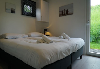 Helles Schlafzimmer in einer Lodge mit Doppelbett, frischer Bettwäsche, Handtüchern und Gartenausblick.