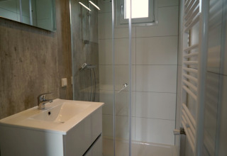 Modernes Badezimmer in einer Lodge mit Dusche, Waschbecken, Fenster und Handtuchheizung, hell gestaltet.