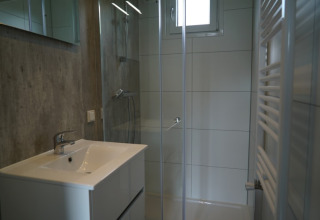 Baño moderno en un lodge con ducha, lavabo, pequeña ventana, puerta de cristal y radiador toallero.
