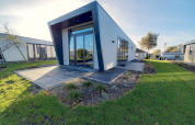 Moderne lodge met schuindak, grote glazen ramen en groen gazon onder een helderblauwe lucht.